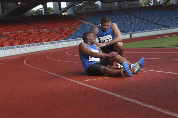 Hombre Atleta Tendido Pista Apretando Pierna Dolor Otro Atleta Ayudando — Foto de Stock