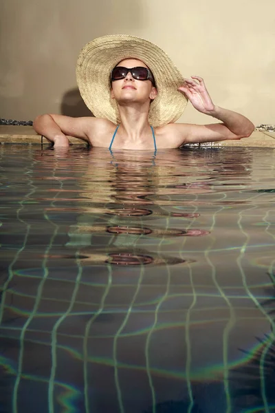 戴着太阳镜和帽子的女人在游泳池里放松 — 图库照片