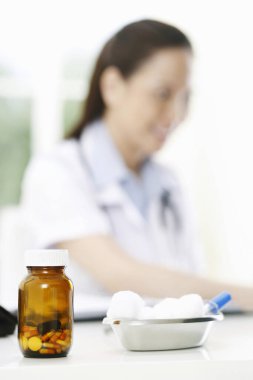 Kadın bir doktorun masasında bir şişe hap ve pamuklu bez.