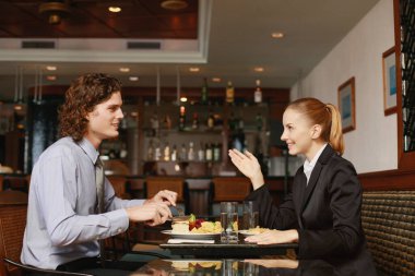 İş adamı ve iş kadını bir restoranda yemek yiyorlar.