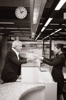 Havaalanı kayıt gişesinde iş adamının pasaportunu iade eden havayolu kayıt görevlisi.