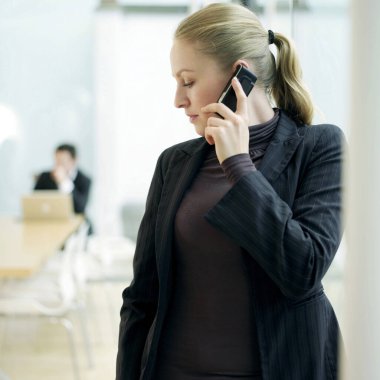 Cep telefonu kullanan bir kadın, arkada oturan bir adam.