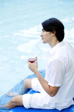 Havuz kenarında kırmızı şarap içen bir adam.