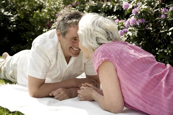 Senior man and woman rubbing nose while lying forward on picnic blanket