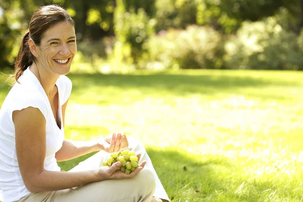 緑のブドウを持って畑に座っている女性 — ストック写真