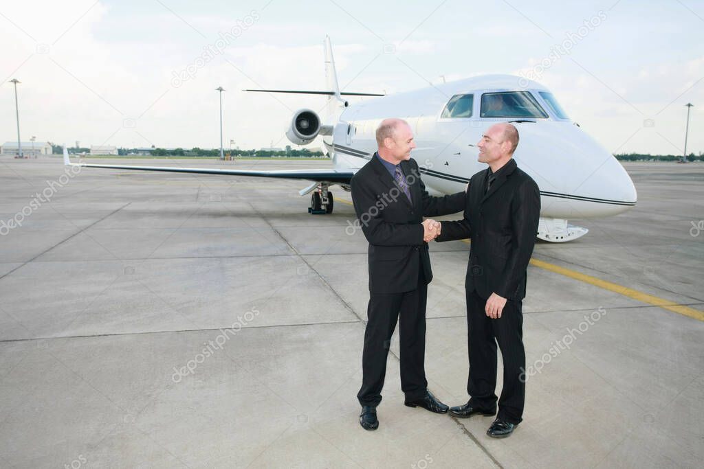 Businessmen shaking hands on runway with private jet in the background