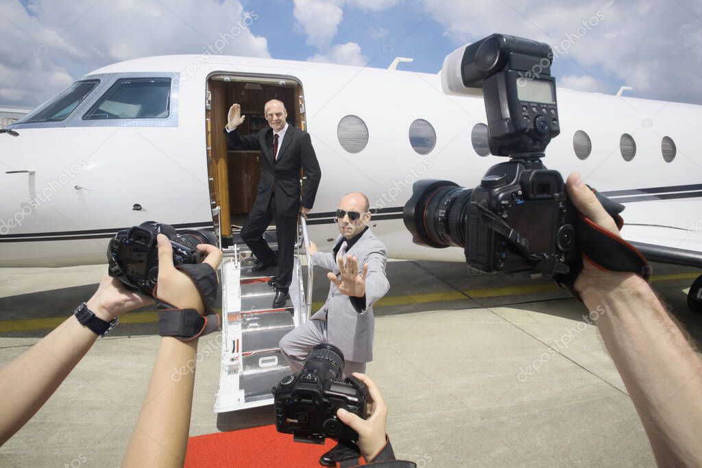 Businessman descending from private jet with his bodyguard, paparazzi taking photographs