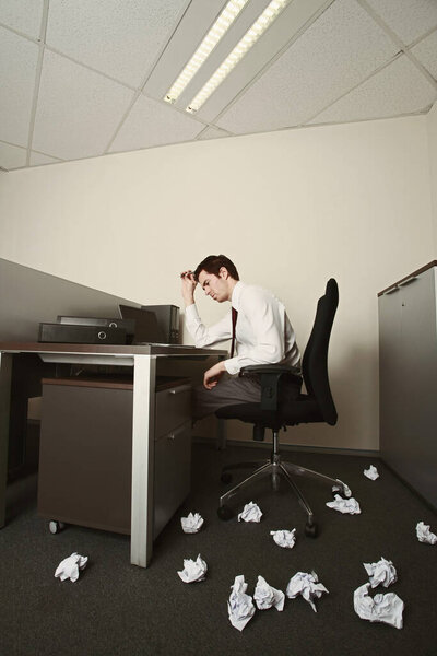 Бизнесмен думает, скомканные бумаги разбросаны по полу
