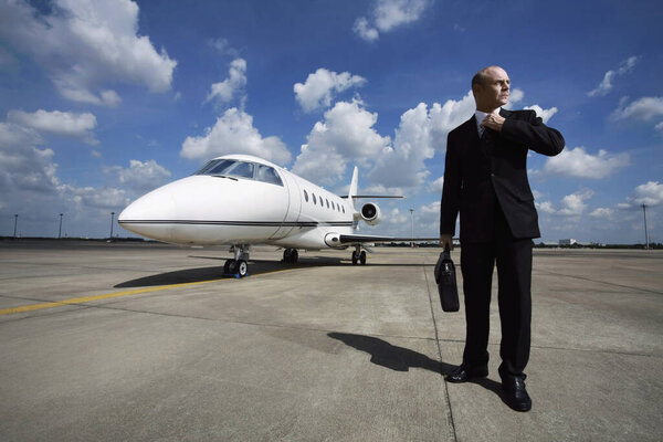 Businessman adjusting his tie on runway with private jet in the background