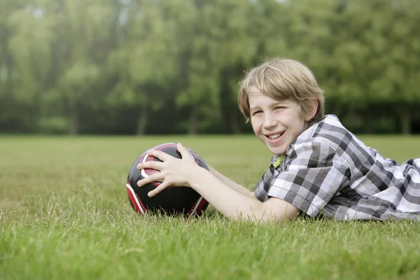 男孩带着足球向前躺在球场上 — 图库照片