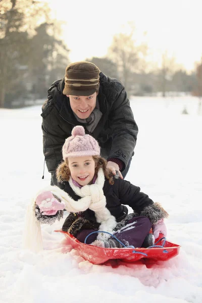父亲把女儿推上雪橇 — 图库照片
