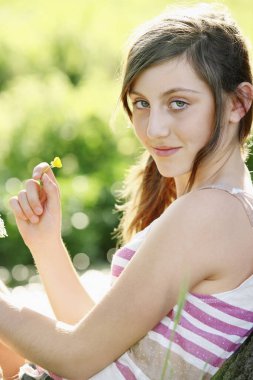 Küçük bir çiçek tutarken kameraya gülümseyen kız