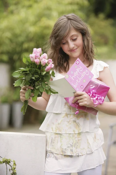 Girl holding a bouquet of flowers and present while reading birthday card