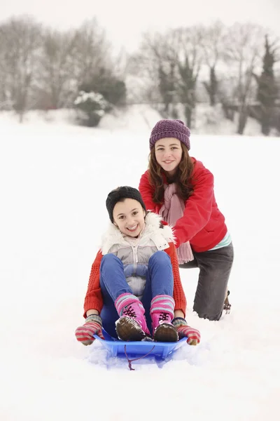 两个女孩在雪地里玩耍 骑着雪橇 — 图库照片