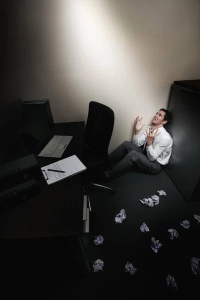 Businessman sitting and crying, crumpled papers scattered on the floor