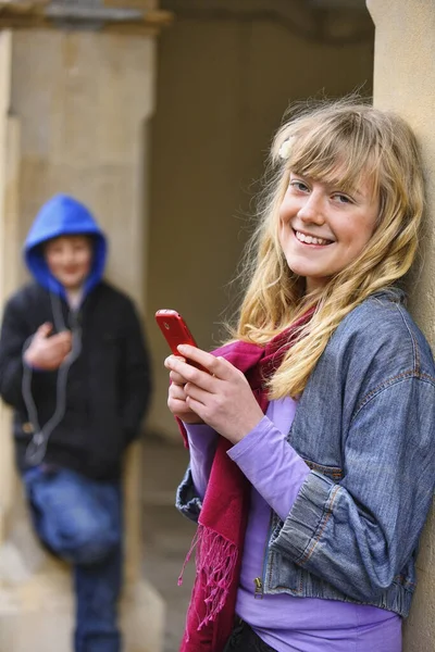 Girl sending a text message while boy listens to music in the background