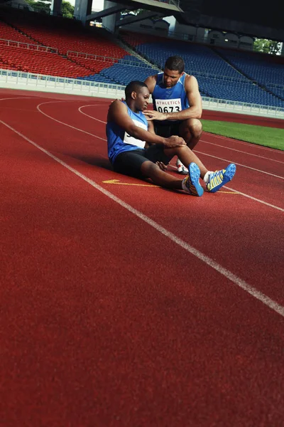 Hombre Atleta Tendido Pista Apretando Pierna Dolor Otro Atleta Ayudando — Foto de Stock