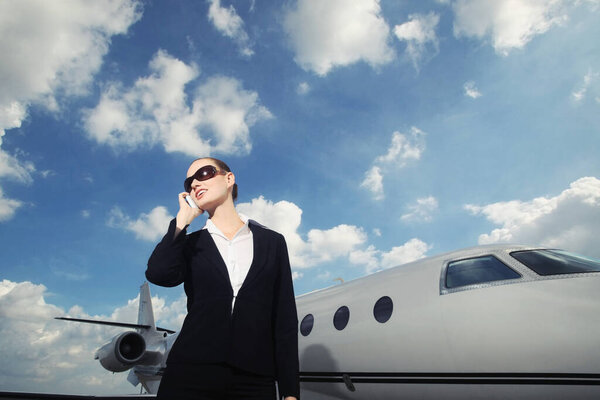 Businesswoman talking on the phone with private jet in the background