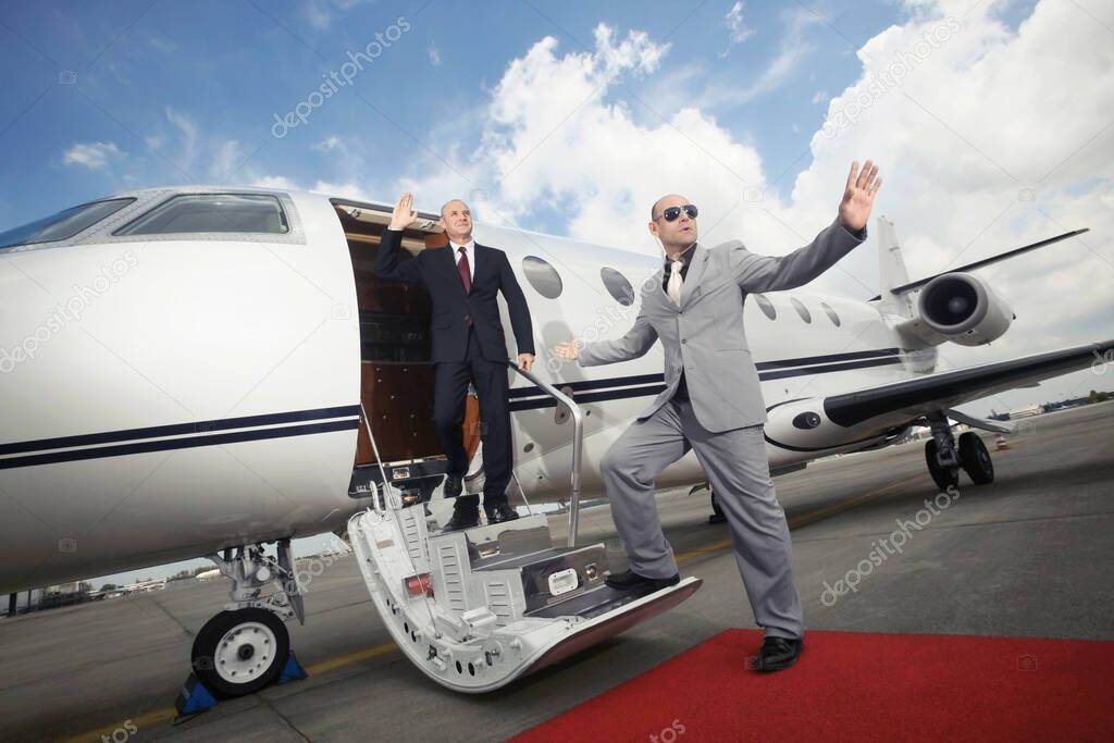 Businessman descending from private jet with his bodyguard