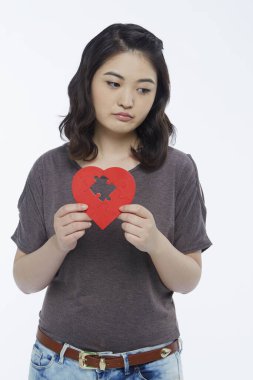 Sad woman holding up a red heart shape with a missing puzzle piece clipart