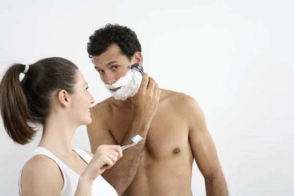 Woman about to brush her teeth with man shaving