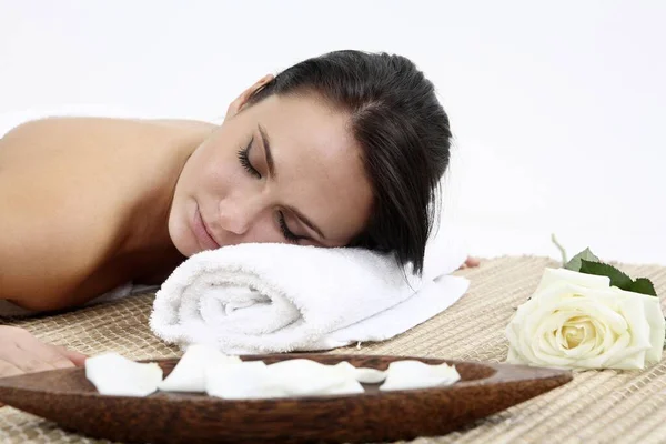 女人躺在一条毛巾上 旁边有一朵玫瑰花和花瓣 — 图库照片