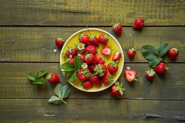 Olgun çiftlik çilekleri sarı bir tabakta yaprakların arasında ve yeşil ahşap bir zemin üzerinde çiçekler yeşil ahşap bir masanın üstünde seramik sarı bir tabakta taze sulu çilekler, üst manzara, kopyalama alanı