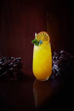 Koyu parlak ahşap zemin üzerinde kuru bir dilim portakal, taze limon otu, nane ve buz küpleriyle bir bardak limonata, kopyalama alanı, boş alan, dikey görüntü