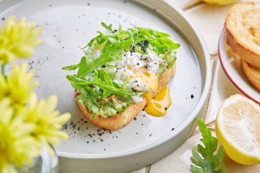 Yaz çiçeklerinin arasında haşlanmış yumurta ve taze roka tabağında guacamole ekmekli tost, sağlıklı aperatif, yaz kahvaltısı, öğle yemeği veya atıştırmalık, yumurta sarısı.