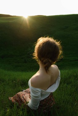 Dağ tepesinde gözleri kapalı otururken akşam güneşi kadınların üzerinde parlıyor kızıl saçlar.