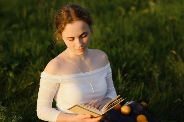 Jovencita leyendo un libro en la hierba mientras se pone el sol. Sensación de verano — Foto de Stock