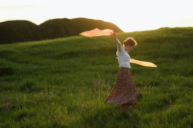 Güzel kızıl saçlı kız gün batımında bir tarlada dans edip eğleniyor.