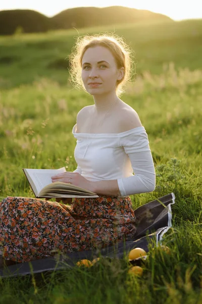 Jovencita leyendo un libro en la hierba mientras se pone el sol. Sensación de verano — Foto de Stock