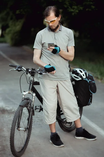 Happy cyclist in a yellow sunglasses using Mobile Phone In Park, Beautiful sunny day — Stock Photo, Image