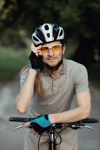 Portret van de mens in een gele zonnebril en helm staand met de fiets op de weg en kijkend in de camera — Stockfoto