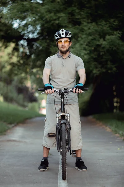 Retrato de homem em óculos de sol amarelos e capacete de pé com bicicleta na estrada e olhando para a câmera — Fotografia de Stock