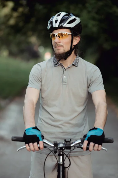 Cyklista ve sportovním oblečení a helmě stojí na silnici v parku a dívá se do strany Royalty Free Stock Obrázky