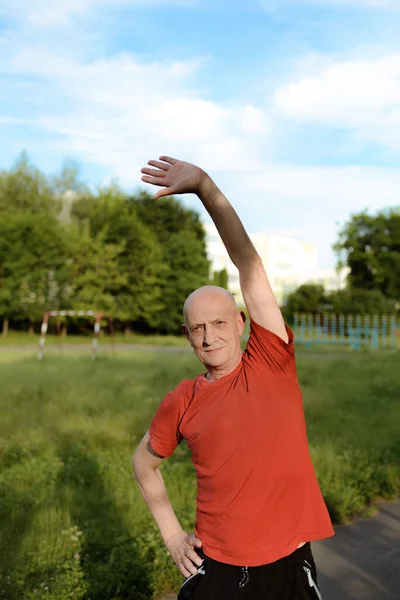 El anciano hace ejercicios en el parque. Estilo de vida activo y saludable . — Foto de Stock