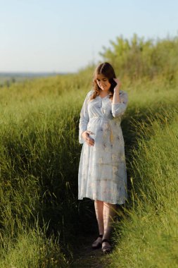 Gün batımında poz veren hamile kadının yan görüntüsü. Hamile kadın karnına hafifçe dokunuyor..