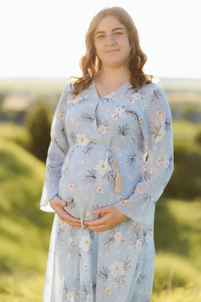 Close up de uma mulher grávida esperando vestindo um vestido azul e segurando sua barriga e relaxante ao ar livre — Fotografia de Stock
