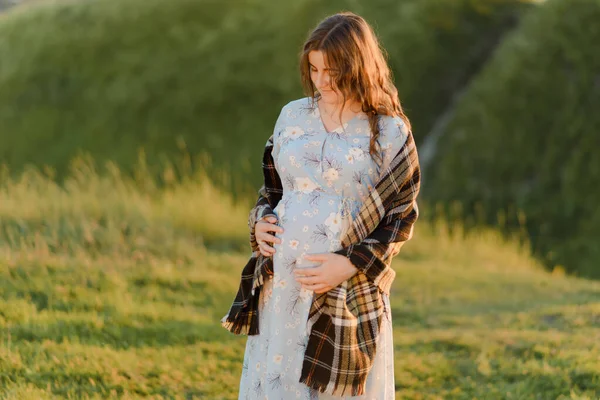 Jonge mooie vrouw zwanger legt haar handen op haar buik en kijkt ernaar met Liefde. Pasgeboren — Stockfoto