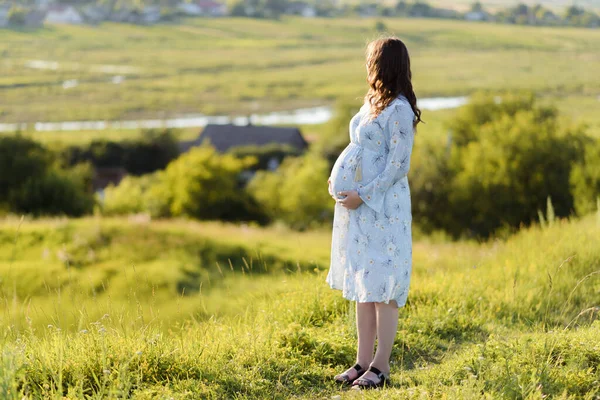 Close up de uma mulher grávida esperando vestindo um vestido azul e segurando sua barriga e relaxante ao ar livre — Fotografia de Stock