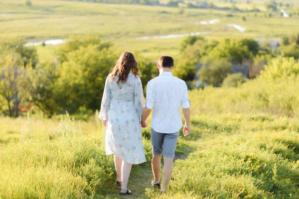 Mujer embarazada cogida de la mano con su marido durante un paseo por el campo al atardecer . —  Fotos de Stock