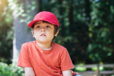 Baharda ya da yaz aylarında parkın derinliklerine bakan yakışıklı bir çocuğun, ağaçların altında oturmuş bulanık yeşil orman arka planıyla tek başına dinlenen bir çocuğun portresi.