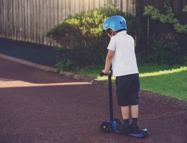 Dikiz aynasındaki çocuk yolda paten sürüyordu, yalnız bir öğrenci scooter 'ın üzerinde dikiliyordu ve yola bakıyordu, üzgün otizmli çocuk tek başına oynuyordu, zihinsel hastalıklı çocuk konsepti.