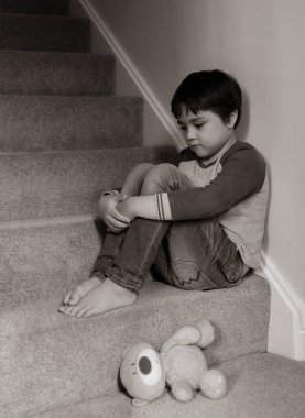 Sad kid sitting on staircase with teddy bear lying down on carpeted in house, Preschool boy looking down with upset face not happy to go back to school, Black and white image, Mental health concept clipart