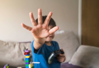 Çocuğun el iç çekmesini durdur, çocuk elinde video oyun konsolu tutarken dur hareketi yapıyor. Aile içi şiddet ve çocuk istismarı kavramı Uluslararası insan hakları veya mülteci günü kavramı.