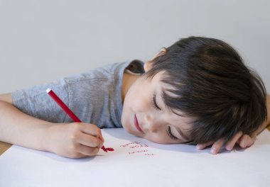 Annesine mesaj yazan mutlu bir çocuğun portresi, kırmızı renkli yazı ve beyaz kağıda çizim yapan anaokulu çocuğu, küçük çocuk, annesi için kırmızı kalbi çizerek masanın üzerine uzanıyor.. 