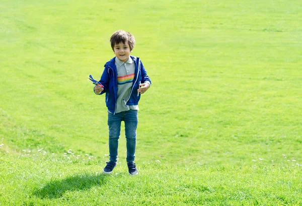 緑の芝生でジャンプする全長のポートレートキッズ プラスチック製の飛行機のおもちゃを遊んでいるかわいい男の子 晴れた日に春や夏のフィールドで屋外で遊ぶことを楽しんでいる子供 — ストック写真