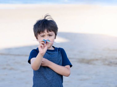 Oyuncak uçakla oynayan mutlu çocuk bulanık kumsalda arka planda, köpük uçak fırlatan çocuk, yazın deniz kenarında oynayan çocuk, çocukluk aktivitesi..